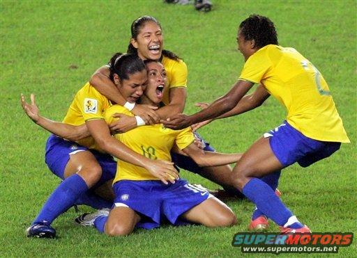 Soccer players in yellow and blue uniforms celebrating on a grass field. Watermark reads SUPERMOTORS