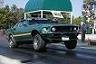 Green muscle car, looks like a 1969 Mustang, but heavily modified with a lifted suspension and different grille