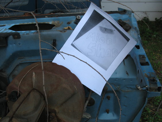 Drawing of 'The Miobi Shop' on paper placed on a rusted blue car's engine bay