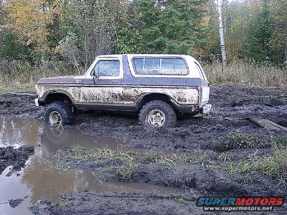 1978 Ford Bronco stuck in a muddy puddle with trees in the background