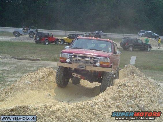 Red Ford F-Series truck with a custom bumper navigating a dirt obstacle