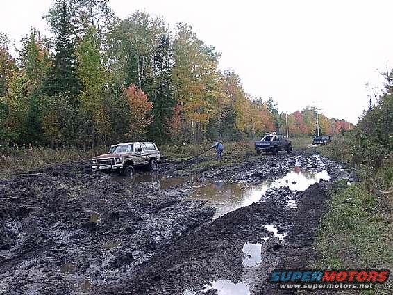 1978 Ford Bronco stuck in deep mud on a trail, another truck visible in background