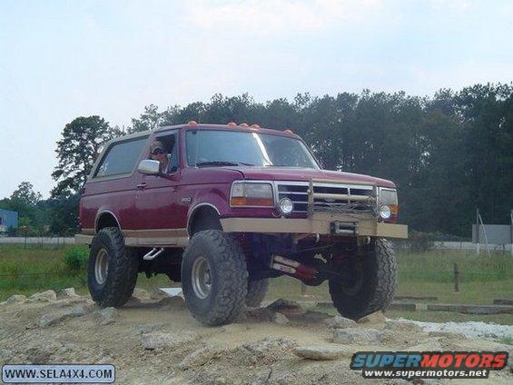 Red lifted 1995 Ford Bronco with aftermarket bumper and winch on rocky terrain