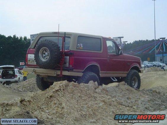 Red and tan Ford Bronco with spare tire on rear bumper, driving over dirt mounds