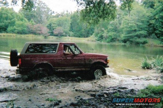 1995 Ford Bronco driving through shallow water and mud, spare tire mounted on rear door