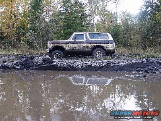 1978 Ford Bronco stuck in a muddy puddle with trees in the background
