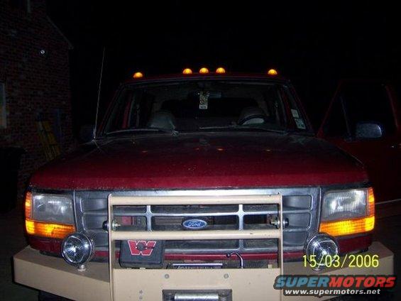 Front view of a red Ford pickup truck with a brush guard and aftermarket lights. It has amber marker lights on the roof