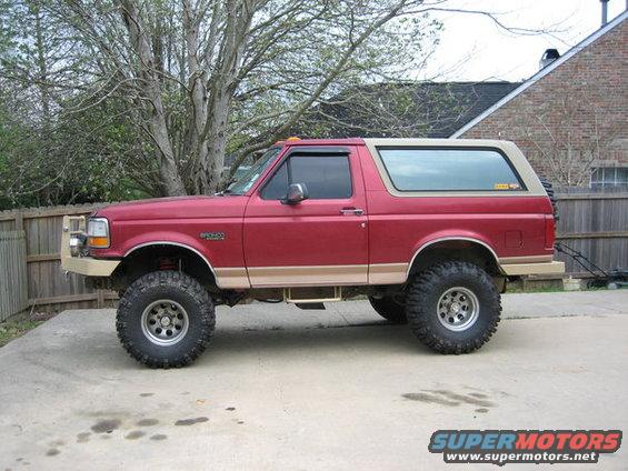 Red Ford Bronco with tan trim, lifted suspension, and large off-road tires, viewed from the side