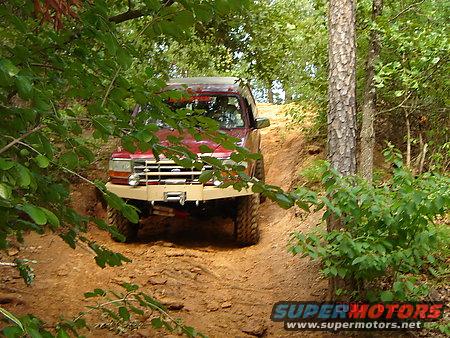 1995 Ford Bronco driving up a steep dirt trail through trees