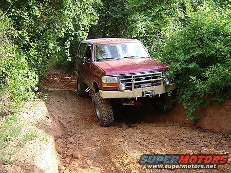 Maroon Ford Bronco with tan aftermarket bumper and winch driving on a muddy trail