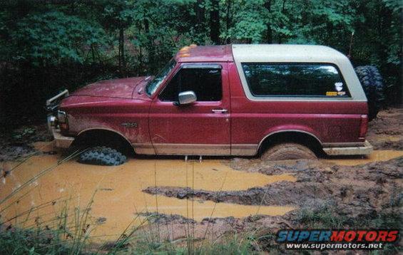 Red 1995 Ford Bronco stuck in deep mud with trees in background