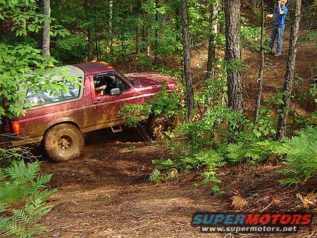 Red off-road SUV with a removable top, mud-splattered, on a dirt trail