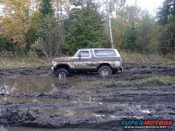 1978 Ford Bronco stuck in mud pit with trees in background