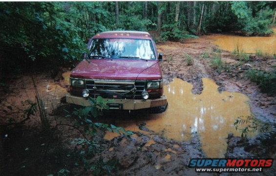Red 1995 Ford Bronco stuck in a muddy puddle in a forest