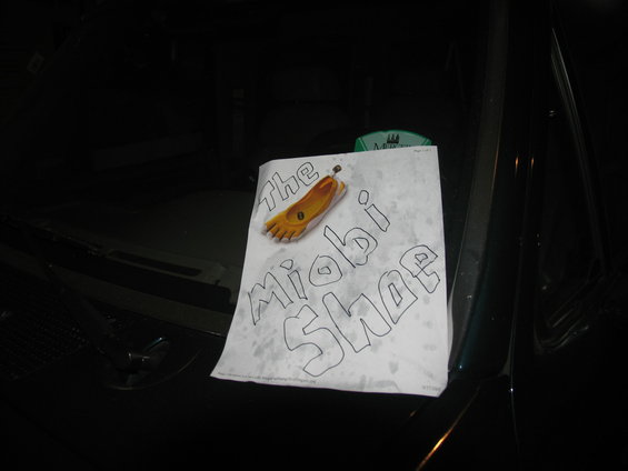 Paper with 'the Miobi Shoe' drawing on dark vehicle hood