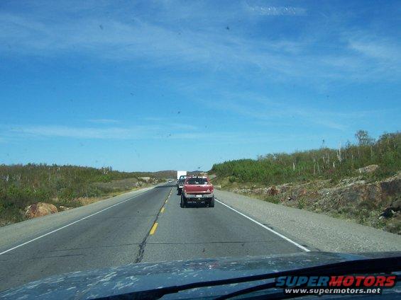 Red pickup truck driving on a highway with a white truck behind it