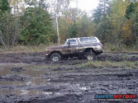 1978 Ford Bronco stuck in deep mud with trees in background