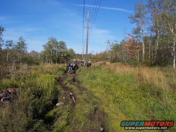 Two off-road vehicles stuck in mud on a trail with power lines overhead