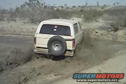 White 1995 Ford Bronco rear view driving through mud with spare tire mounted