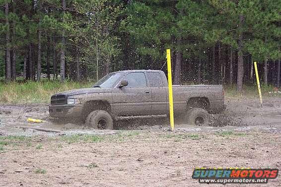 Mud-covered pickup truck stuck in mud with yellow poles nearby