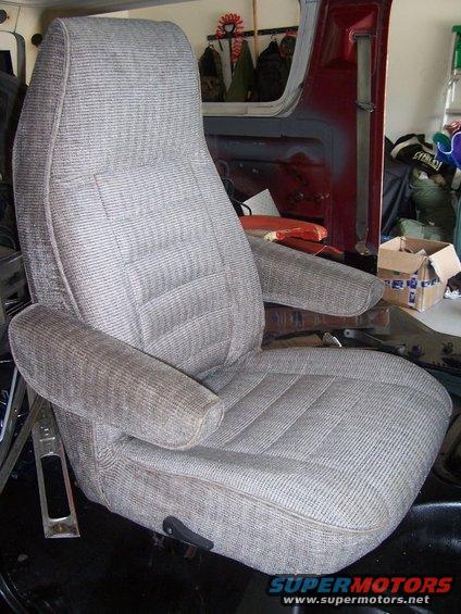 Gray fabric vehicle seat with armrests, inside a vehicle with red interior panels visible