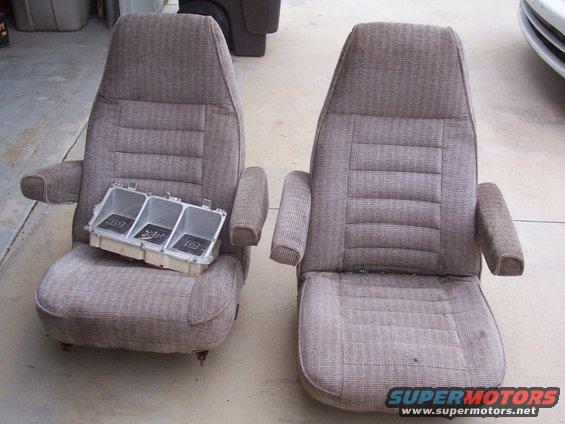 Two brown fabric car seats with armrests, one with a silver gauge cluster housing