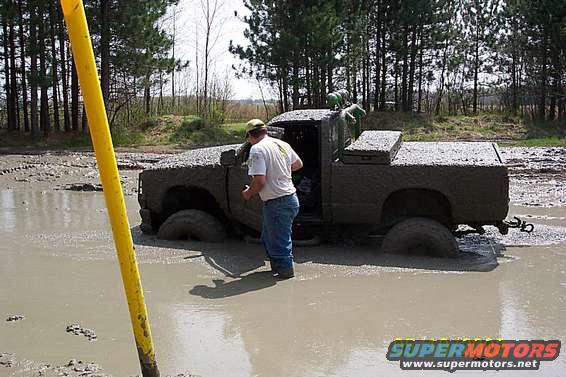 Mud-covered pickup truck stuck in a muddy field with a person standing next to it