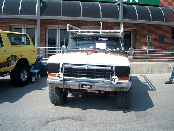 Front view of a lifted 1970s Ford F-Series truck with custom paint. A yellow Ford Bronco is parked to the left