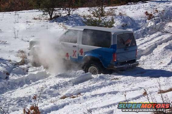 White and blue Ford Bronco II with red 4x4 graphics driving in snow, kicking up dust