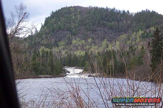 Water flows over rocks in a river with a forested mountain in the background
