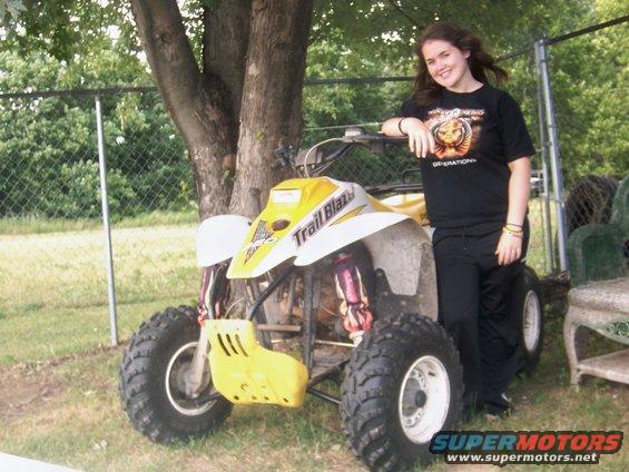 Yellow and white all-terrain vehicle with 'Trail Blaze' text on the side, parked on grass next to a tree