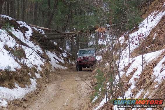 Jeep Wrangler driving on a muddy, snowy trail through a forest
