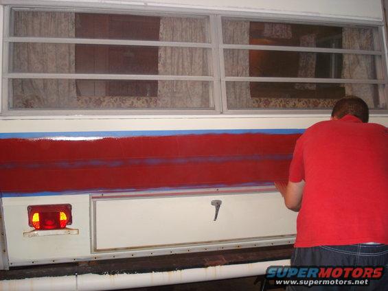 Camper side with red stripe being painted, blue tape visible
