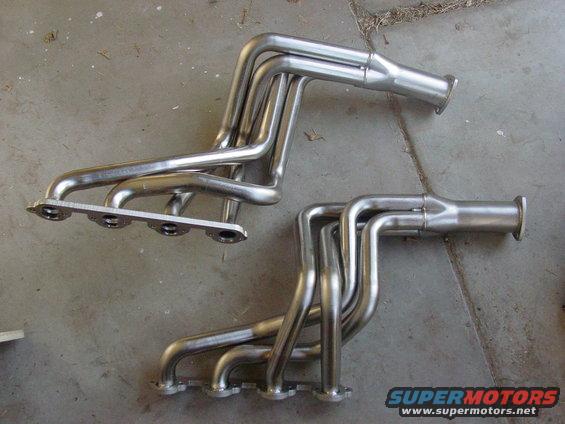 two sets of shiny metal exhaust headers on a concrete surface