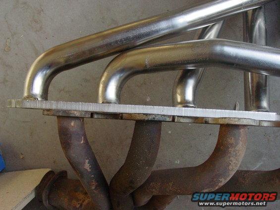Exhaust manifold with shiny pipes and rusty pipes attached to a metal plate