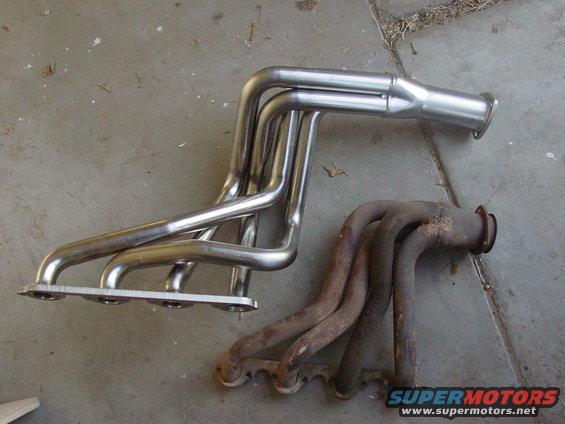 Two exhaust manifolds, one shiny and new, the other rusty and old, on a concrete surface