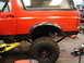 1989 Ford Bronco - Side view of a red SUV with off-road tires, partially raised on a yellow hydraulic lift.