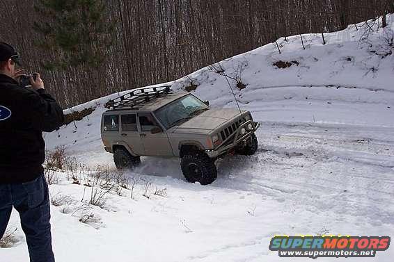 Tan Jeep Cherokee XJ with roof rack driving in snow, front bumper modified
