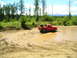 1989 Ford Bronco - Red pickup truck stuck in mud on a dirt road with trees and sky.