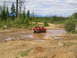1989 Ford Bronco - 1989 Ford Bronco navigating a muddy obstacle course with trees and mountains in the background.