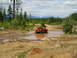 1989 Ford Bronco - A red pickup truck navigates through a muddy off-road course with trees and hills in the background.