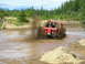 1989 Ford Bronco - A red pickup truck navigates a muddy off-road course, sending dirt and water flying.