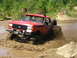 1989 Ford Bronco - A red Ford Bronco navigates a muddy off-road course, kicking up a spray of mud.