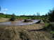1989 Ford Bronco - Two trucks navigate a challenging muddy terrain under a clear blue sky.