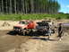 1989 Ford Bronco - Two modified trucks are parked in a dirt lot with trees behind them.