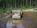 1989 Ford Bronco - Two trucks navigate a challenging muddy terrain, surrounded by a dense forest.