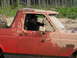 1989 Ford Bronco - A driver sits in a heavily muddied red Ford Bronco, its body style indicating a 1987 model year.