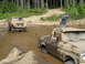 1989 Ford Bronco - Two off-road trucks are stuck in the mud and water, with one vehicle attempting to tow the other.