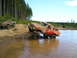 1989 Ford Bronco - Two modified pickup trucks tackle a challenging muddy water crossing in a wooded area.