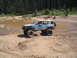 1989 Ford Bronco - A lifted blue Jeep Cherokee XJ navigates an off-road course with a muddy puddle nearby.